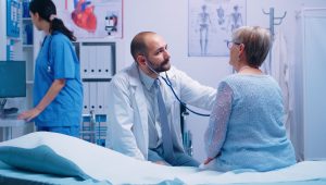 elderly woman doctor appointment modern private clinic while she sitts hospital bed physician is listening her heart beat health care medicine treatment specialist consultation scaled