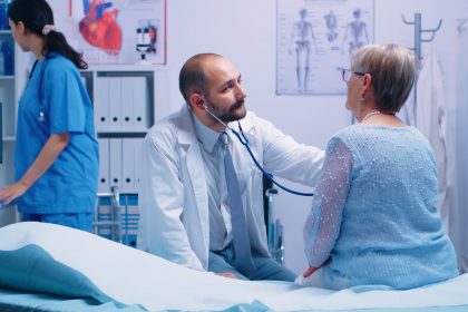 elderly woman doctor appointment modern private clinic while she sitts hospital bed physician is listening her heart beat health care medicine treatment specialist consultation scaled